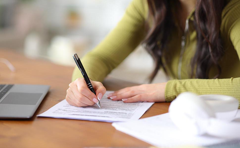 Close up portrait of student hands filling out form on a wooden table at home